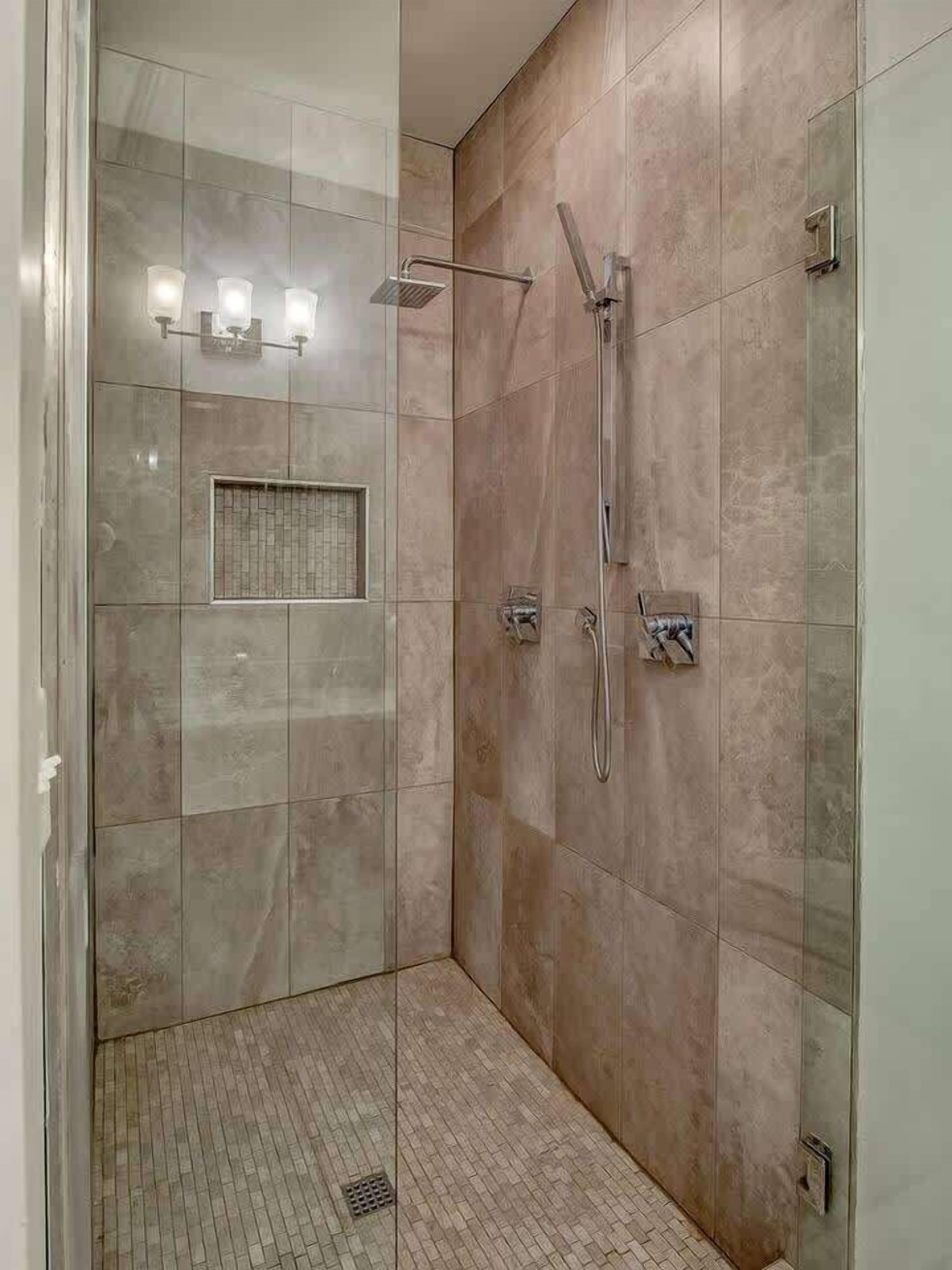 A walk-in shower with a glass door, a wall-mounted towel rack, and a rectangular vent.