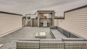 A rooftop patio with a built-in grill, a seating area, and a view of the cityscape.
