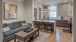 A modern kitchen with a central island, bar stools, and a dining area with a sofa and coffee table.