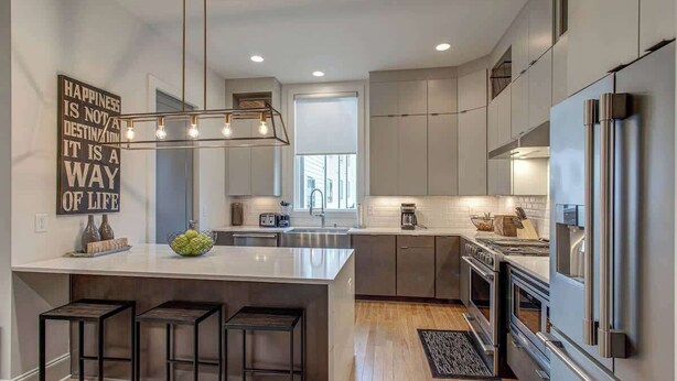 A modern kitchen with a central island, bar stools, stainless steel appliances, and a statement wall with motivational text.