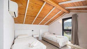 Ein Schlafzimmer mit zwei Betten, Holzbalkendecke, einem Fenster mit Vorhängen und einer Klimaanlage.
