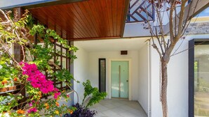 Ein modernes Haus mit einer Holzpergola, üppigem Bougainvillea und einem gefliesten Eingangsbereich.