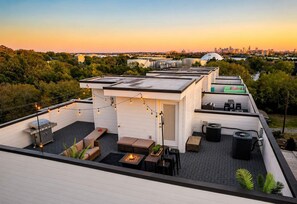 A rooftop terrace with outdoor seating, a grill, and string lights.