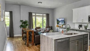 A modern kitchen with a marble island, a dining area with a wooden table and chairs, and a large window with curtains. - Luxury Nashville Rooftop Retreat • Sleeps 12 (Nashville)