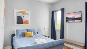 A bedroom with a bed, a bench, a painting, and a window with curtains. - Luxury Nashville Rooftop Retreat • Sleeps 12 (Nashville)