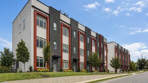 A multi-story residential building with a modern architectural design, featuring a combination of brick and siding exteriors, and a series of windows aligned vertically. - Luxury Nashville Rooftop Retreat • Sleeps 12 (Nashville)