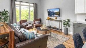A modern living room with a sofa, chairs, a coffee table, a TV, and a kitchen area. - Luxury Nashville Rooftop Retreat • Sleeps 12 (Nashville)