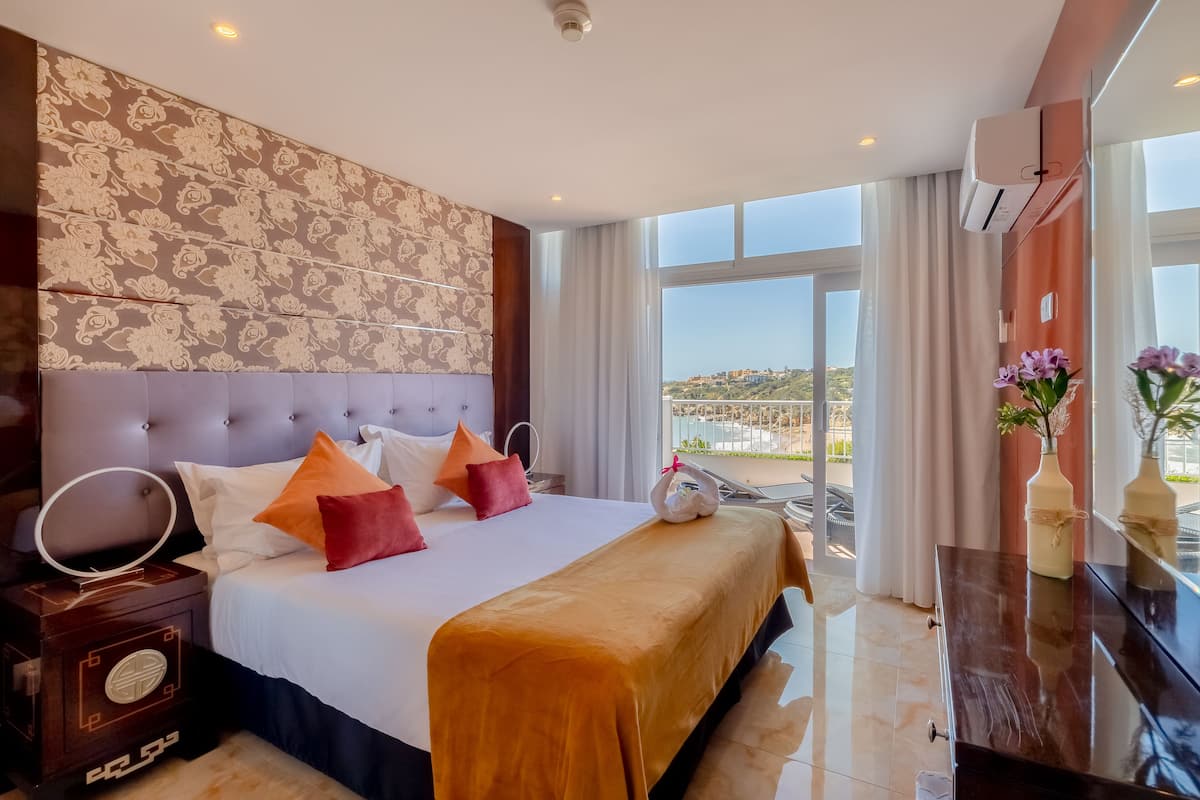 A hotel room with a large bed, a vanity with a mirror, and a view of a cityscape through large windows.