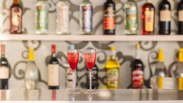 Dos vasos de cóctel rojo sobre una barra con una variedad de botellas de licor al fondo.