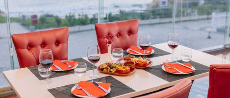 A dining table with red chairs, set with plates, cutlery, and glasses of red wine.