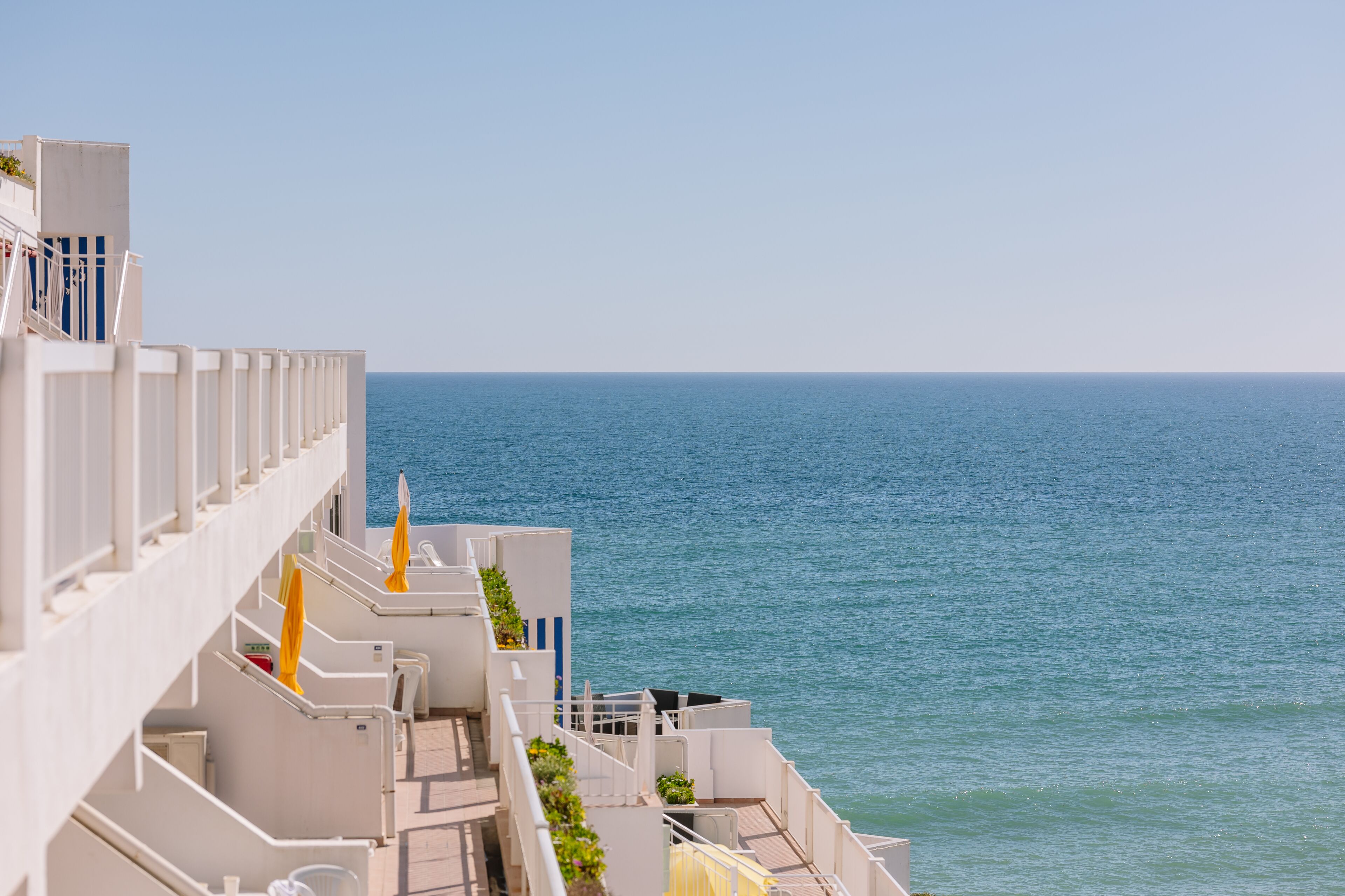 A balcony with a view of the sea, white railings, and yellow umbrellas.