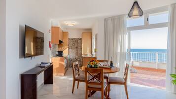 Una sala de estar moderna con comedor, televisor y balcón con vistas al mar.