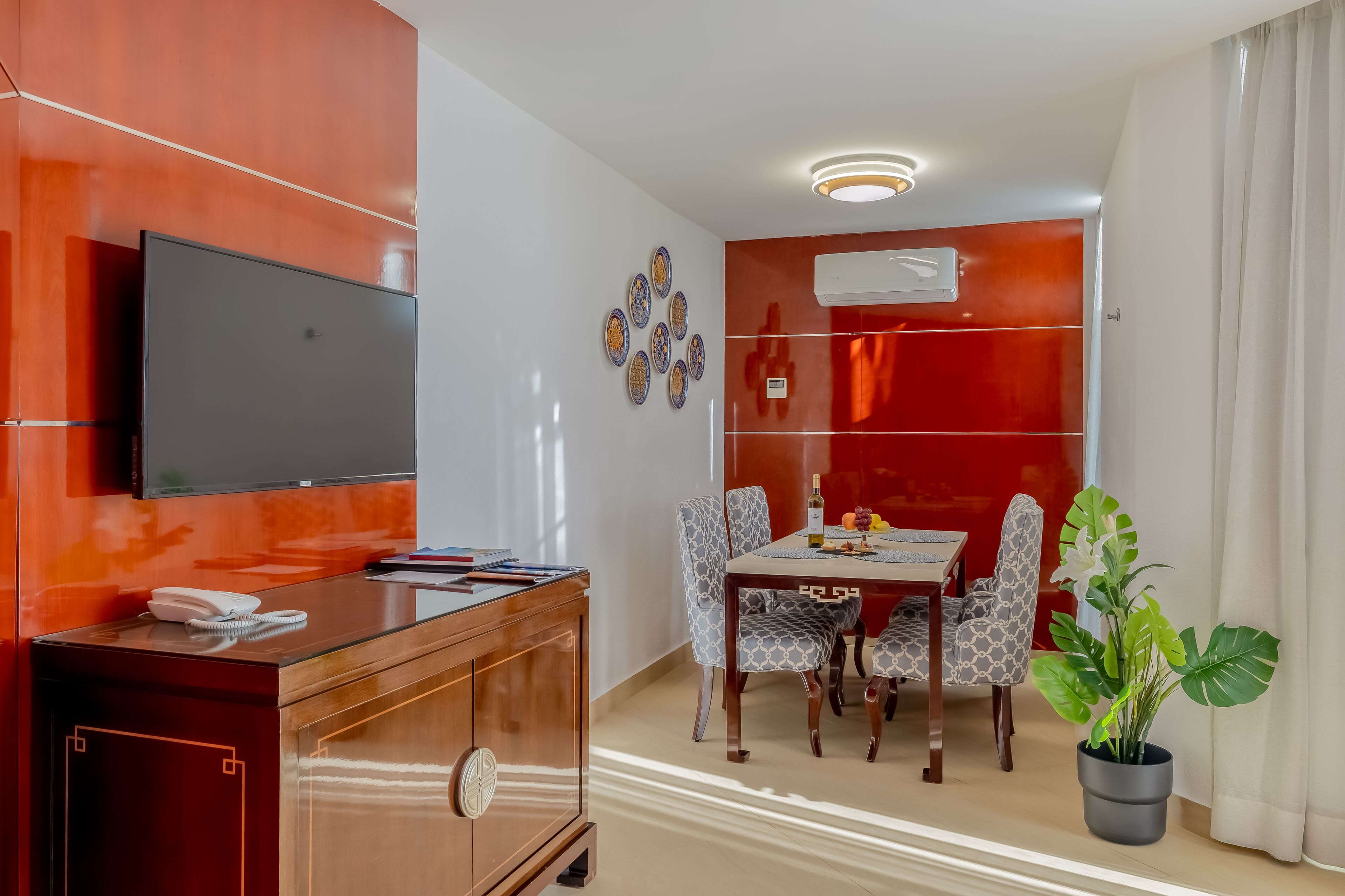 Een moderne hotelkamer met een houten kast, een flatscreen-televisie, een eettafel met gestreept stoelen en een kamerplant.