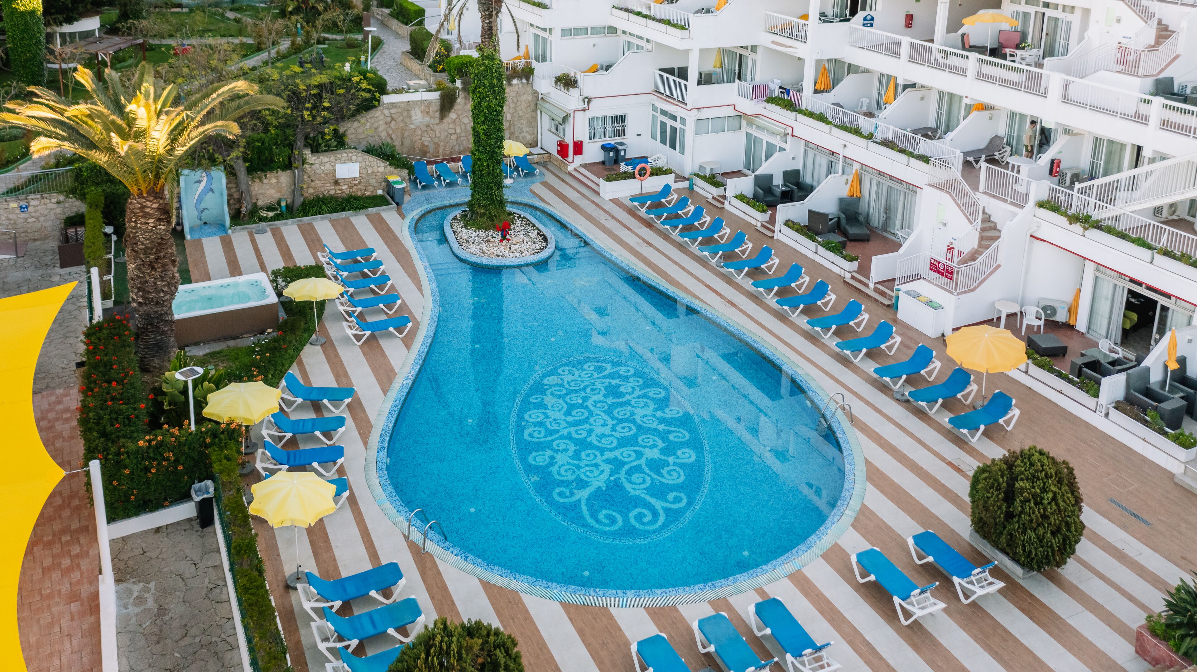 A large pool with a decorative pattern in the center, surrounded by lounge chairs and umbrellas.