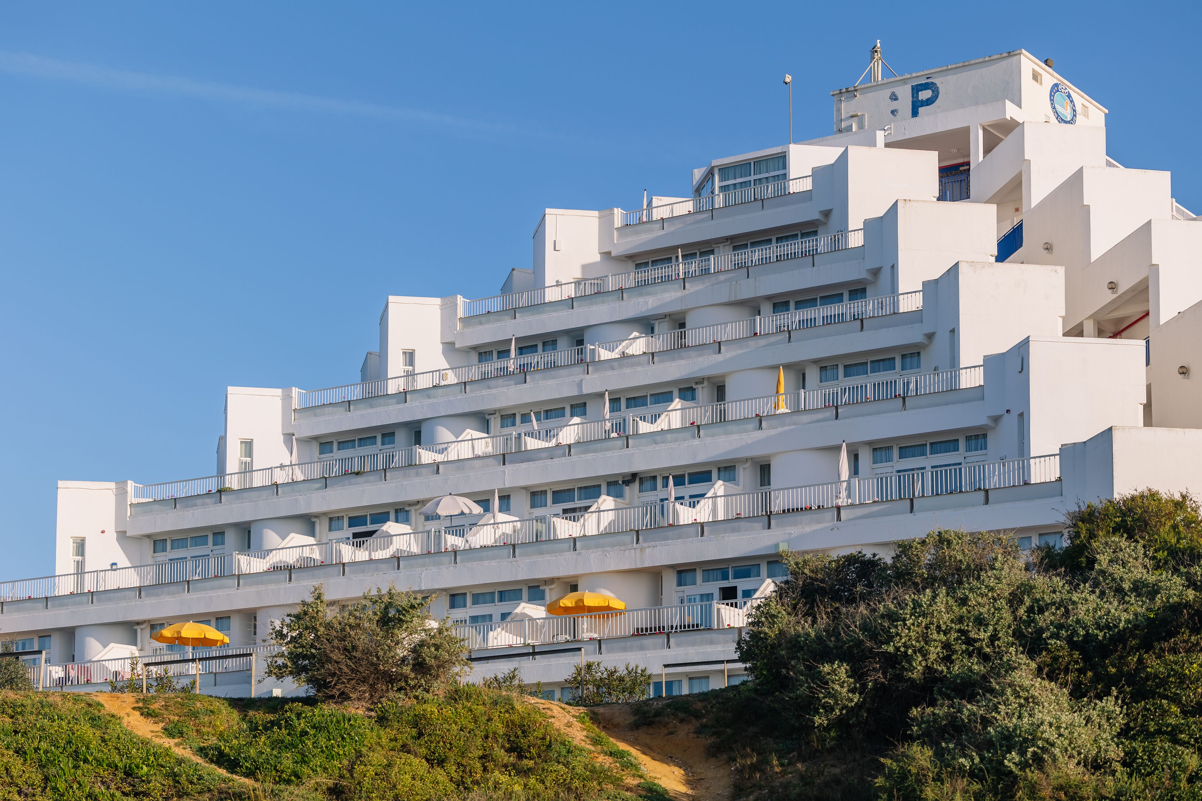 A multi-story hotel with balconies, a prominent 'P' sign, and a clear blue sky.