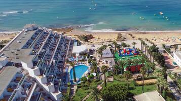 A resort with a pool, beach, and a large building with rows of rooms.