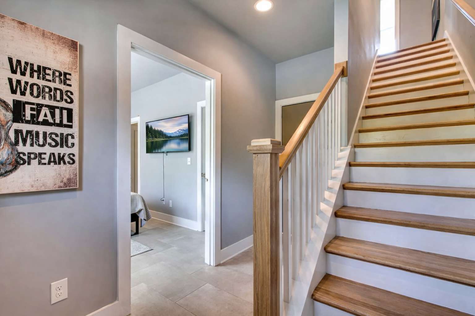 Un couloir avec un escalier en bois, un tableau accroché au mur et un téléviseur dans la pièce adjacente.