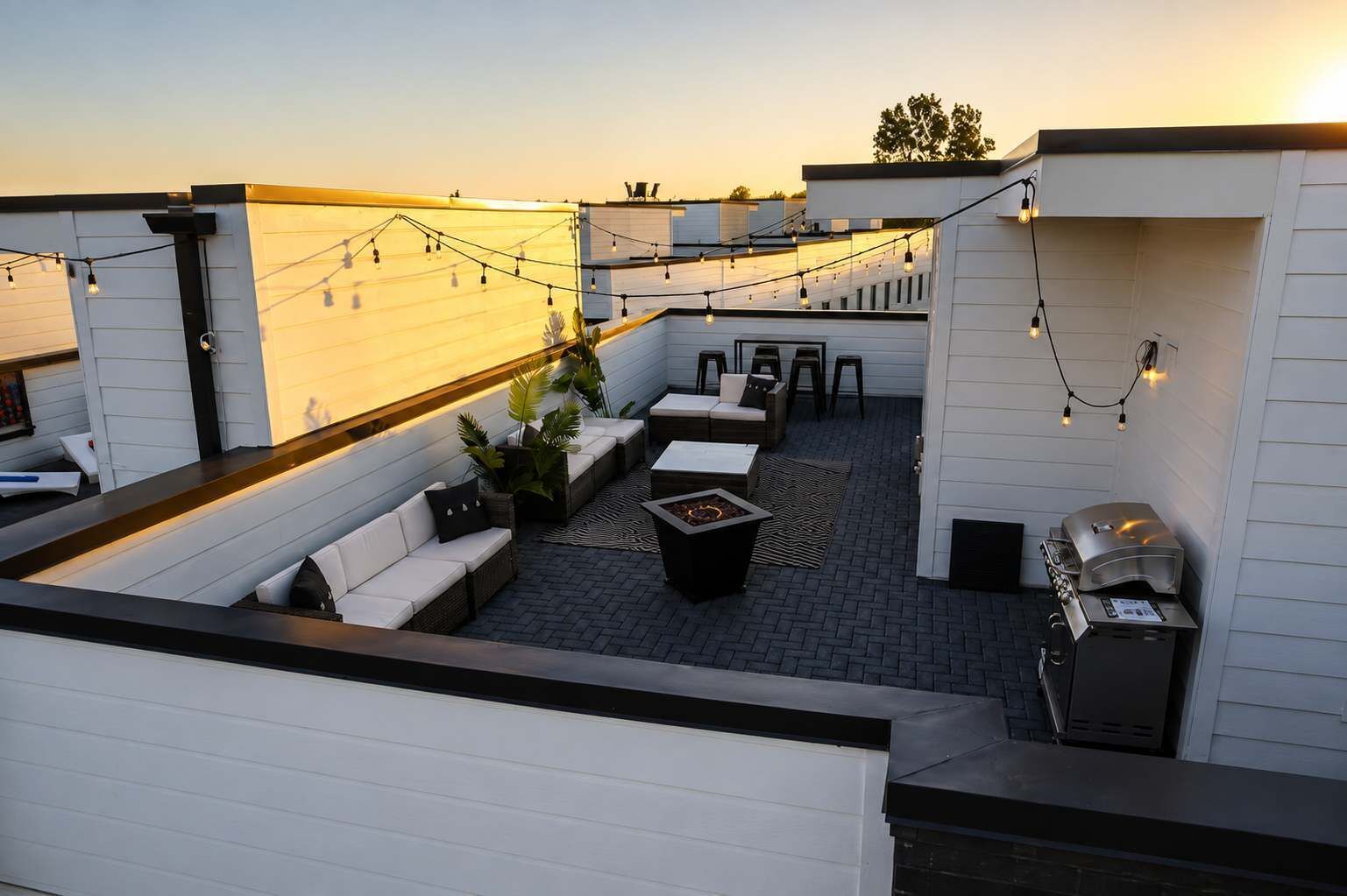 Une terrasse sur le toit avec des sièges extérieurs, un barbecue et des guirlandes lumineuses.