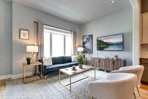 A modern living room with a sofa, coffee table, and chairs, a TV, and a painting on the wall.