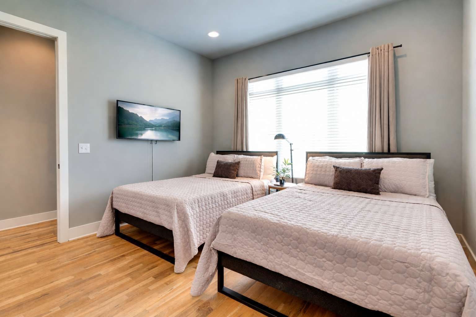 A bedroom with two beds, a TV, and a window with curtains.