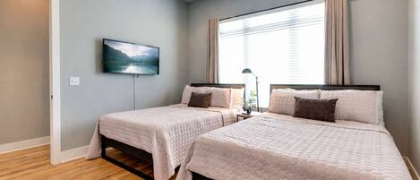 A bedroom with two beds, a TV, and a window with curtains.