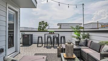 Eine Dachterrasse mit Sitzgelegenheiten im Freien, Lichterketten und Kübelpflanzen.
