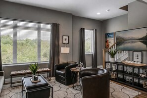 Una sala de estar moderna con un sofá, dos sillones, una mesa de centro, un televisor y una estantería.