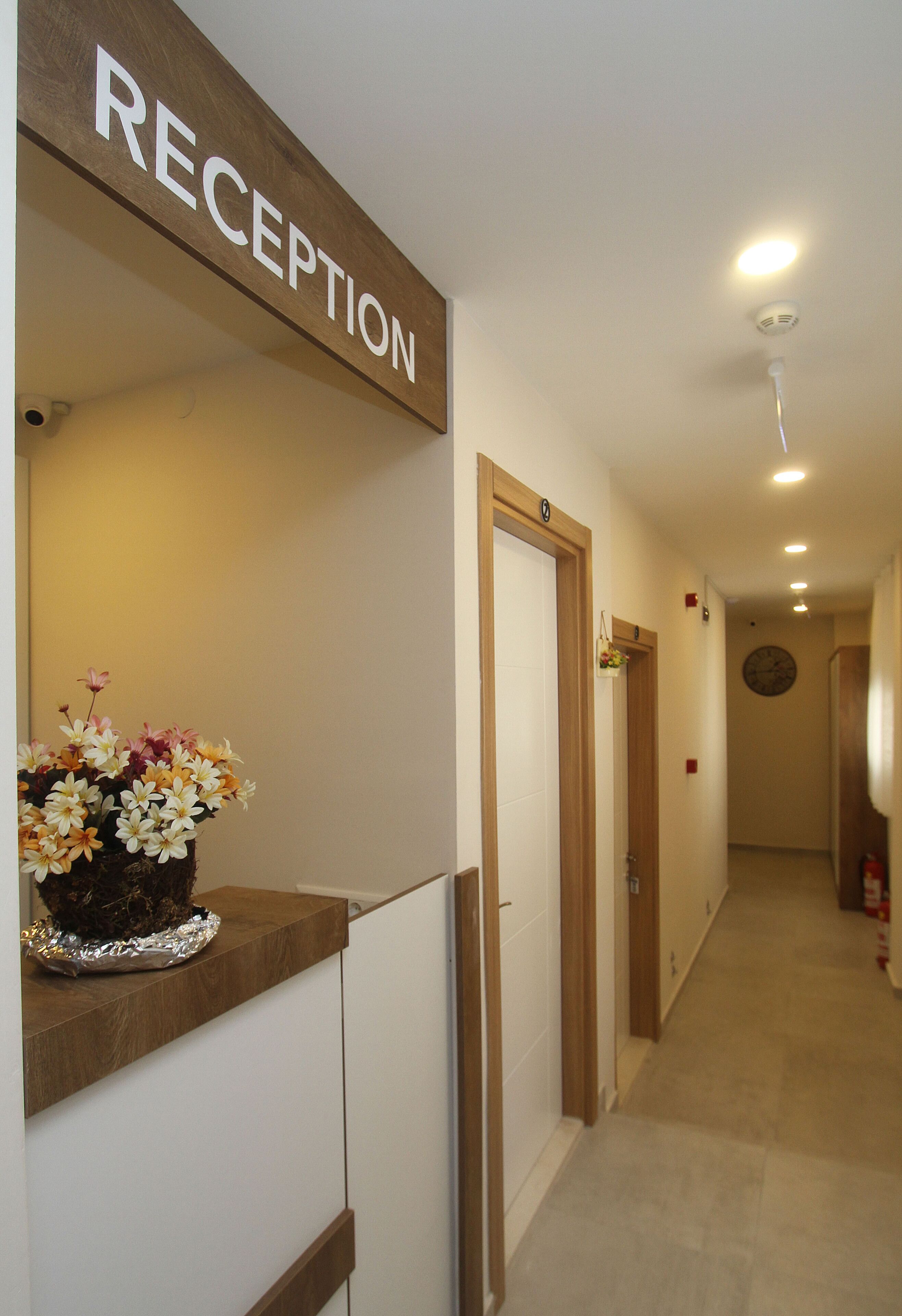 Zona de recepción con un cartel, un arreglo floral y un pasillo que conduce a otras habitaciones.