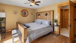 A bedroom with a wooden headboard, a bed with a plaid bedspread, a ceiling fan, and a wooden door. - Lakefront Family Retreat • Dock • Hot Tub & Games (Cadiz)
