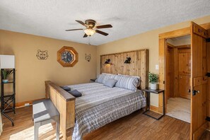 Un dormitorio con cabecera de madera, cama con colcha escocesa, ventilador de techo y puerta de madera.