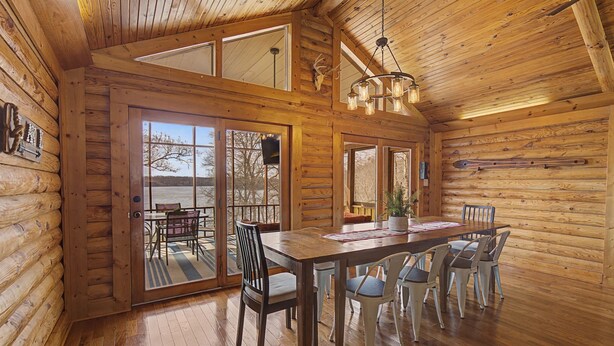 A log cabin interior with a dining area, large windows, and a ceiling light fixture. - Lakefront Family Retreat • Dock • Hot Tub & Games (Cadiz)
