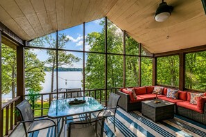 A sunroom with a glass wall overlooking a lake, furnished with a glass table, chairs, and a red sofa. - Lakefront Family Retreat • Dock • Hot Tub & Games (Cadiz)
