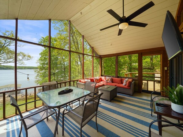 A spacious deck with a glass table and chairs, a red sofa, and a ceiling fan. - Lakefront Family Retreat • Dock • Hot Tub & Games (Cadiz)