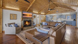 Ein geräumiges Wohnzimmer mit Kamin, einer großen Couch, einem Couchtisch und einer Küche im Hintergrund.