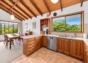 A modern kitchen with wooden cabinets, a dishwasher, and a large window offering a view of greenery.