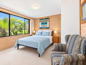 A bedroom with a large window, a bed, a chair, and a painting on the wall.