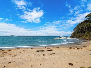 A beach with clear skies, calm sea, and rocky outcrops.