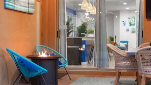 A modern outdoor seating area with a fire feature, wicker chairs, and a view into the interior of the building.