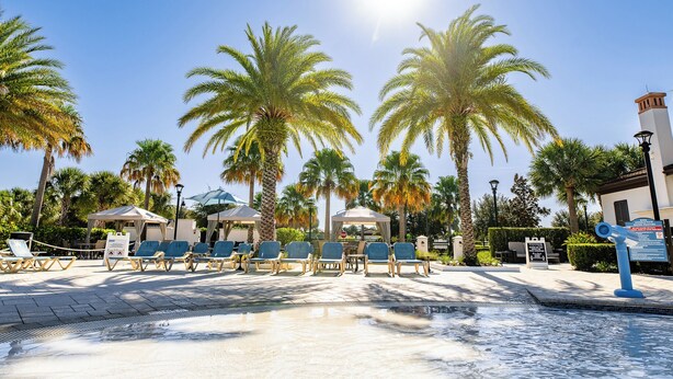 A poolside area with lounge chairs, palm trees, and a clear sky.