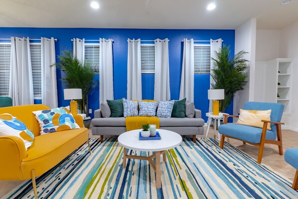 A living room with a sofa, armchair, and coffee table, a blue accent wall, and white curtains.