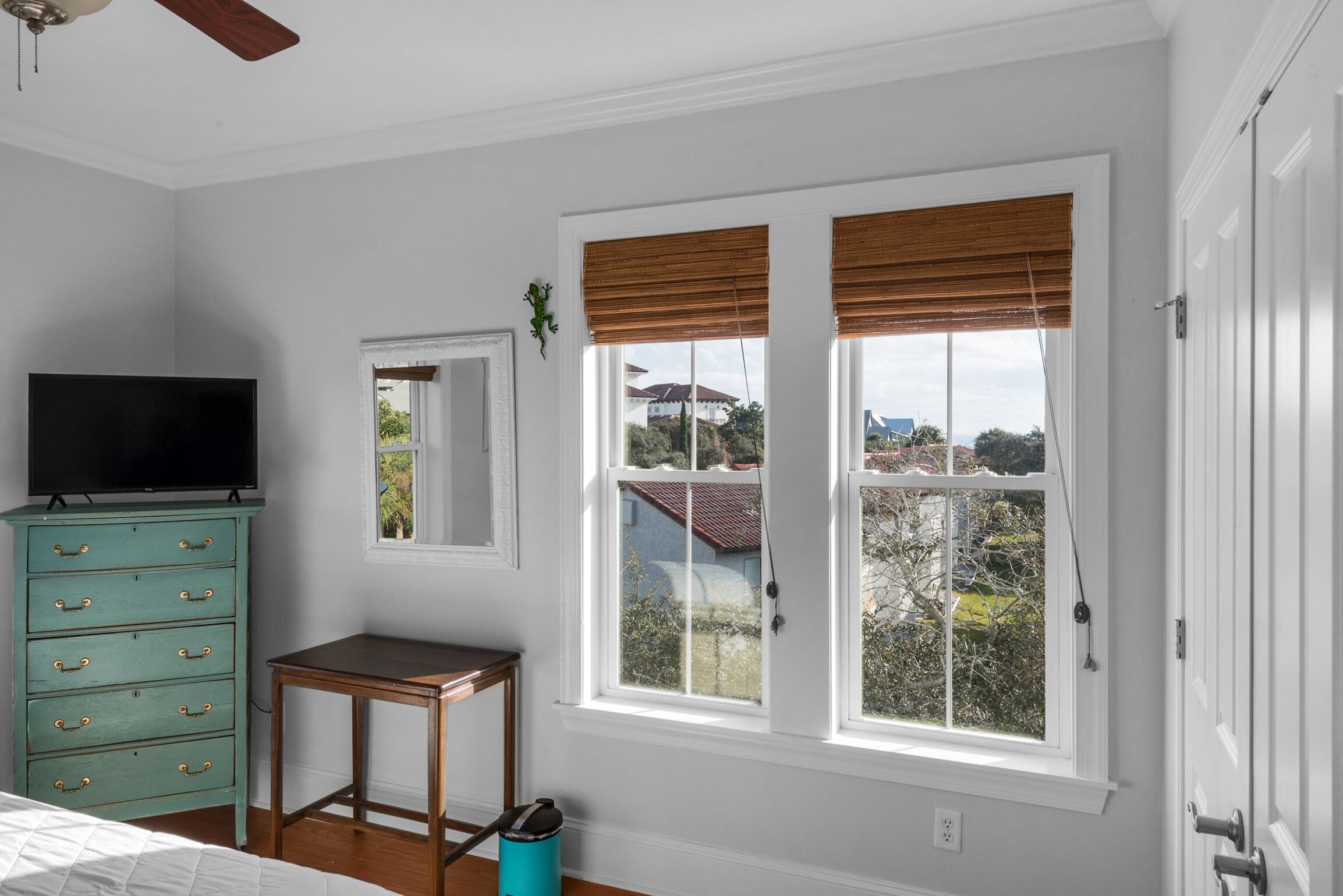 A bedroom with a bed, a dresser, a TV, a window with blinds, and a view of the outside.