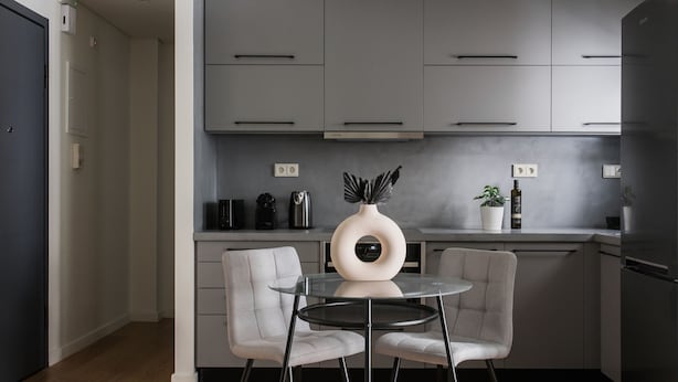A modern kitchen with grey cabinets, a round glass table, two grey chairs, and a decorative vase. - Striking 1BR Apartment in Kolonaki A (Athens)