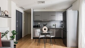 A modern kitchen with grey cabinets, a stainless steel refrigerator, and a round glass table with two chairs. - Striking 1BR Apartment in Kolonaki A (Athens)