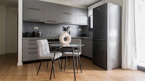 A modern kitchen with grey cabinets, a stainless steel refrigerator, and a round table with chairs. - Striking 1BR Apartment in Kolonaki A (Athens)