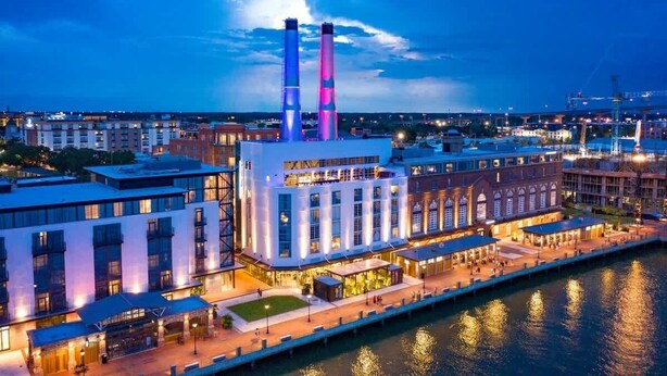 Un hotel frente al agua con diseño moderno, que presenta un edificio central con dos torres destacadas, una zona de embarcadero y vistas al río.