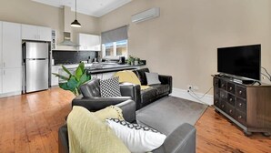Un soggiorno moderno con un divano grigio, una televisione su un mobile, e una cucina sullo sfondo.