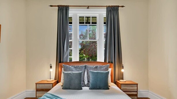 Camera da letto con un letto grande, due comodini, una finestra con tende e vista sul verde.
