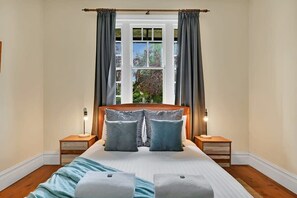 Une chambre avec un grand lit, deux tables de chevet, une fenêtre avec des rideaux et une vue sur la verdure.