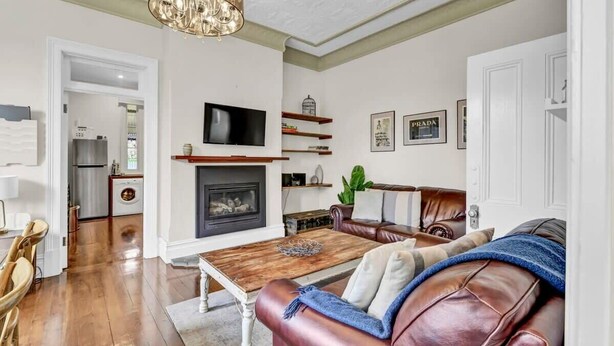 A living room with a fireplace, leather sofa, wooden coffee table, and a chandelier.