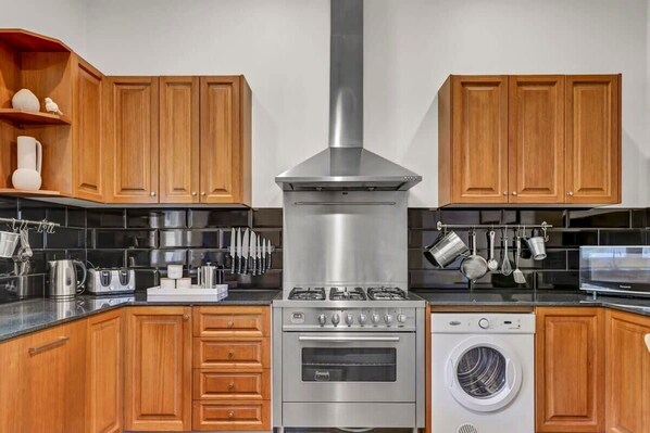 Una cucina moderna con pensili in legno, una cappa in acciaio inossidabile, forno a incasso, lavatrice e un piano di lavoro con diversi utensili da cucina.
